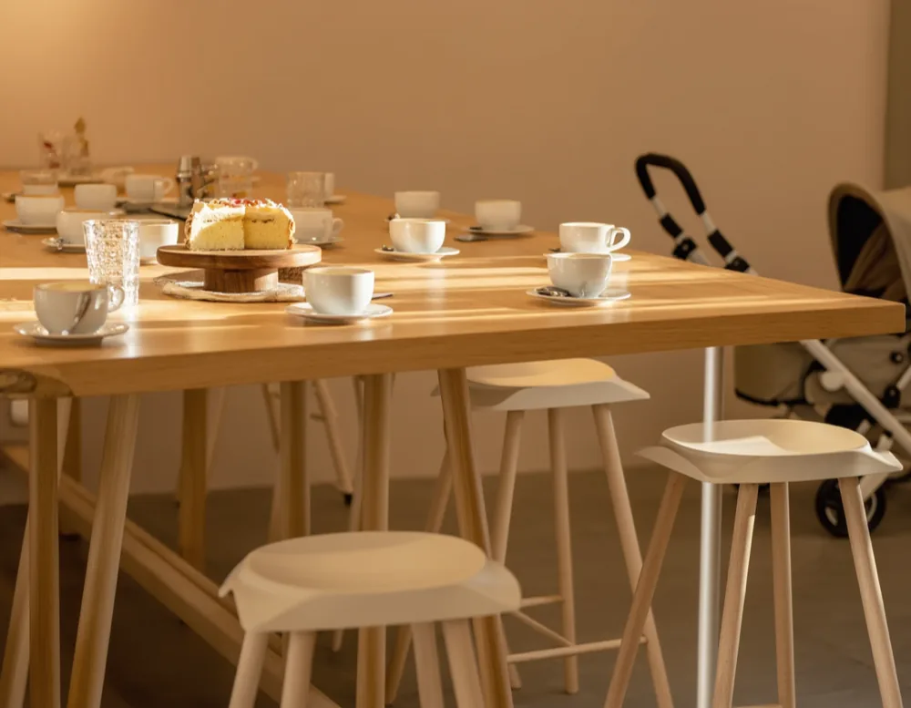 The long communal table set up for Parents' Friday: cake on a wooden stand, a row of cups and glasses, and prams parked behind.